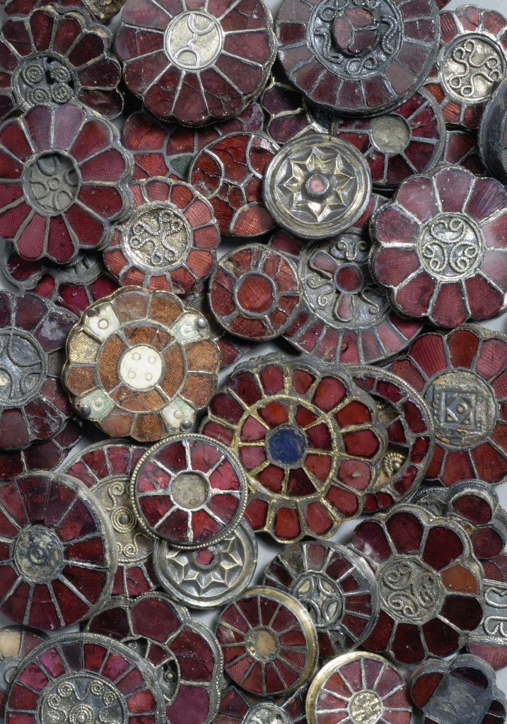 Frühmittelalterliche Gewandnadeln, wie Blüten geformt mit rotem Glas als Blütenblättern. Sie stammen aus der Zeit der Merowingerherrschaft in Bayern.