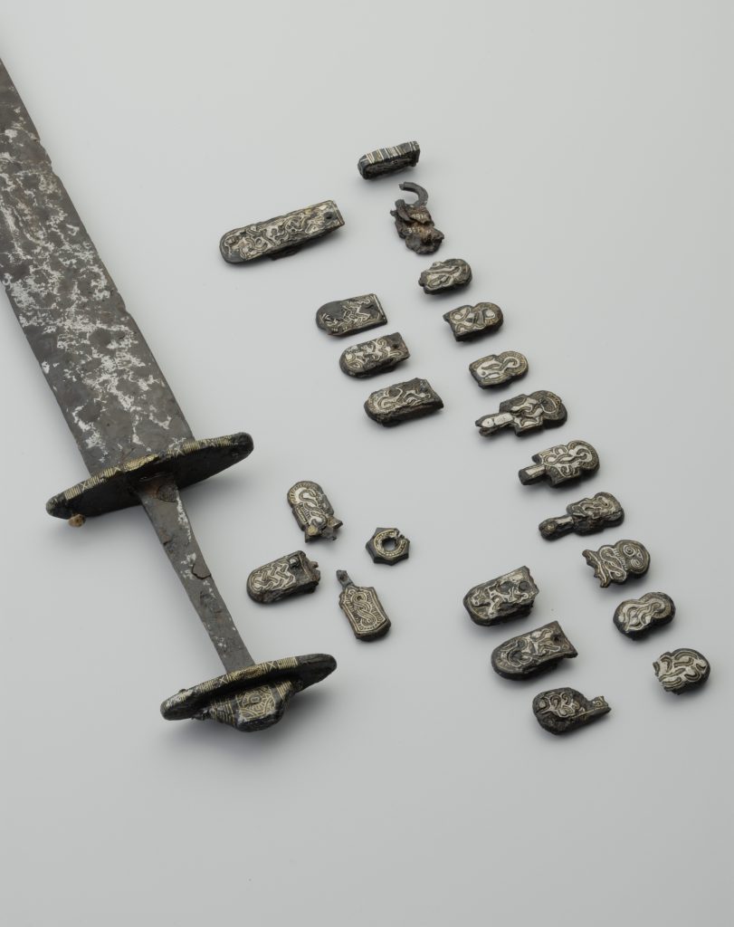 Ein frühmittelalterliches Schwert mit dazu passenden Metallscheiben, die den Gürtel des Schwertträgers verzierten. Die Funde stammen aus der Zeit der Merowingerherrschaft in Bayern.