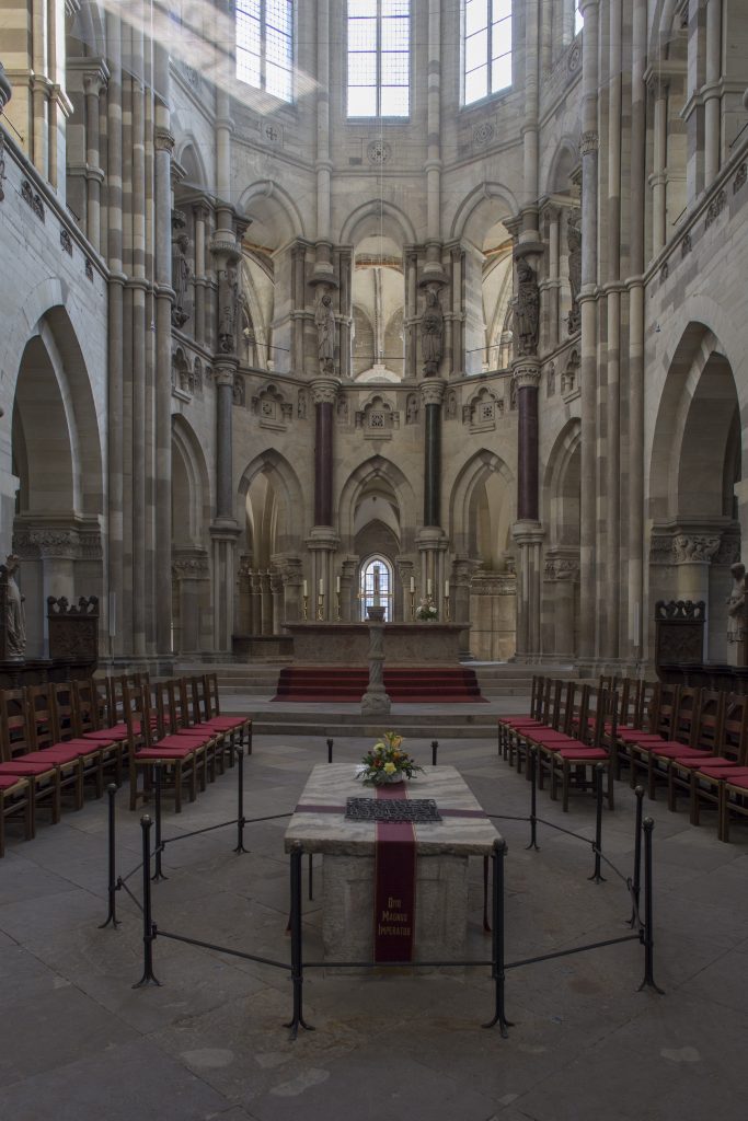 Bild des Chorraums des Magdeburger Doms. Im Vordergund der weiße steinerne Sargkophag von Otto dem Großen. Auf der Marmorplatte eine rote Schleppe mit einem Blumenstrauß.