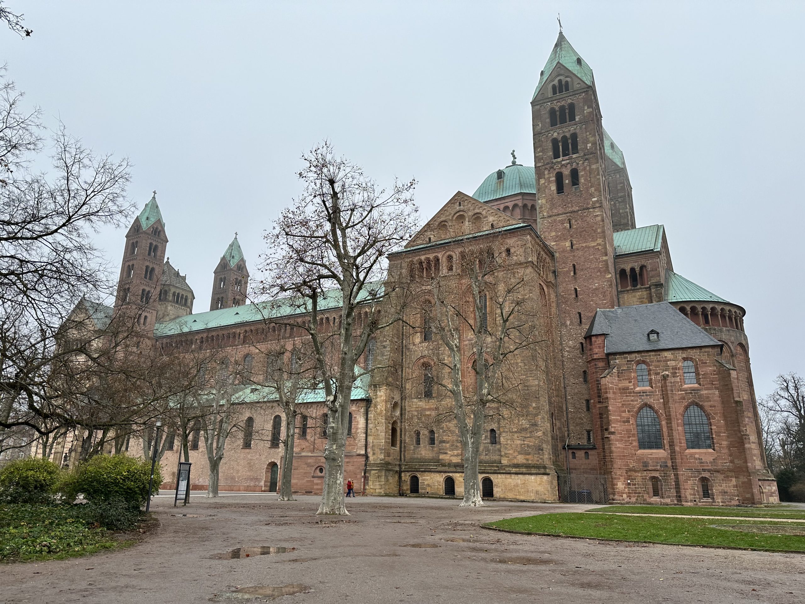 Der Dom zu Speyer von der Westseite fotografiert. Ein monumentaler mittelalterlicher Bau mit vier Türmen, einem großen Querschiff und dem halbrunden Chor. Er ist aus rötlichem Sandsteingebaut. Die Kupferdächer bilden mit ihrer grünen Patina einen schönen farblichen Kontrast.